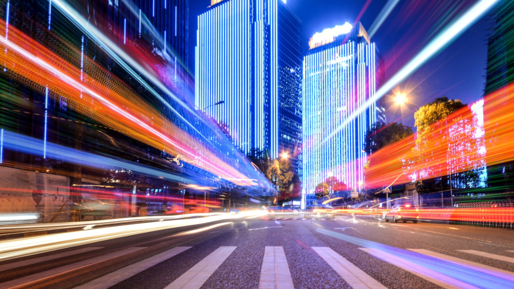 City street at night with vibrant light trails from moving vehicles and buildings illuminated in bright blue lights, symbolizing rapid digital data flow. This visual metaphor emphasizes the speed and efficiency of a fiber internet connection and high-speed fiber internet powered by an enterprise ISP.
