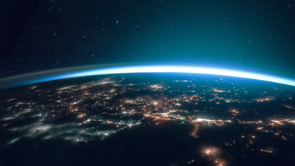A breathtaking view of Earth from space at night, showing illuminated city networks stretching across the surface, symbolizing global connectivity. The planet's curvature glows under a blue atmospheric haze. This image metaphorically represents the reach and integration of business phone systems, connecting enterprises across vast distances seamlessly.