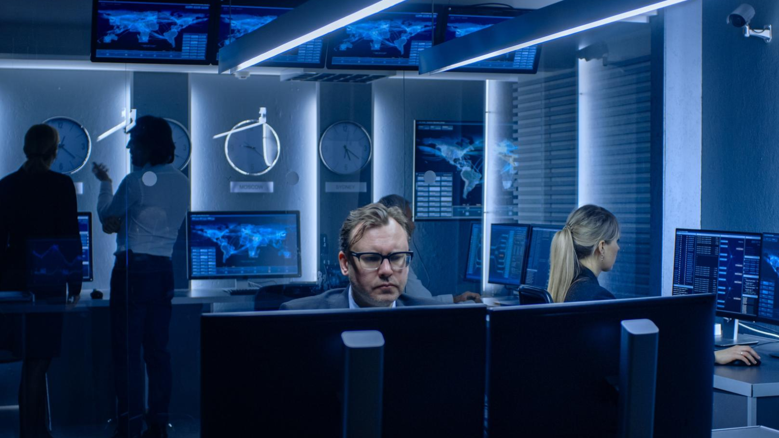 Specialists working in a secure control room with digital world maps and network monitoring tools.
