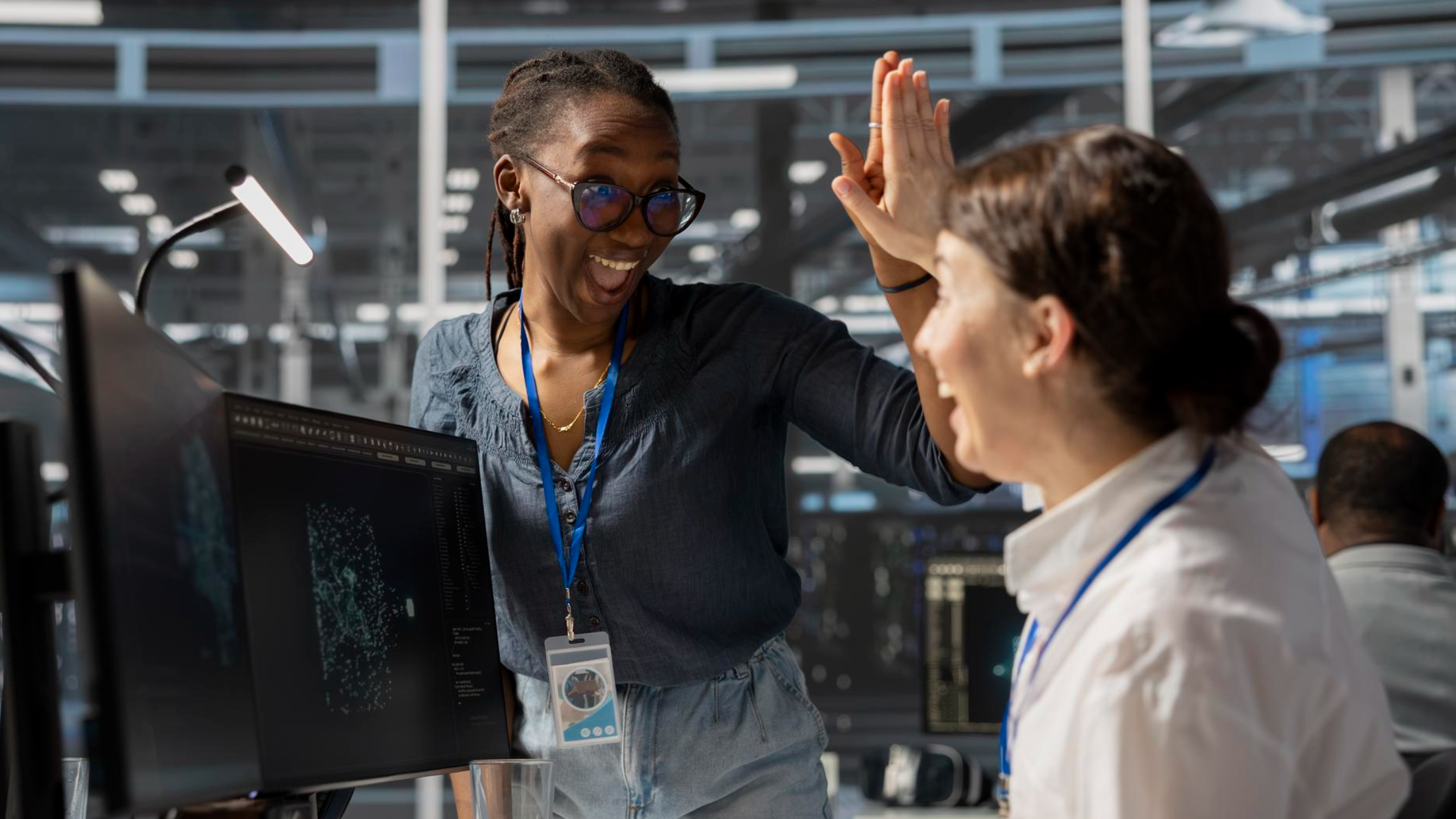 Two coworkers celebrating with a high-five in a NOC, highlighting the teamwork and support system success with a PS Lightwave partnership.