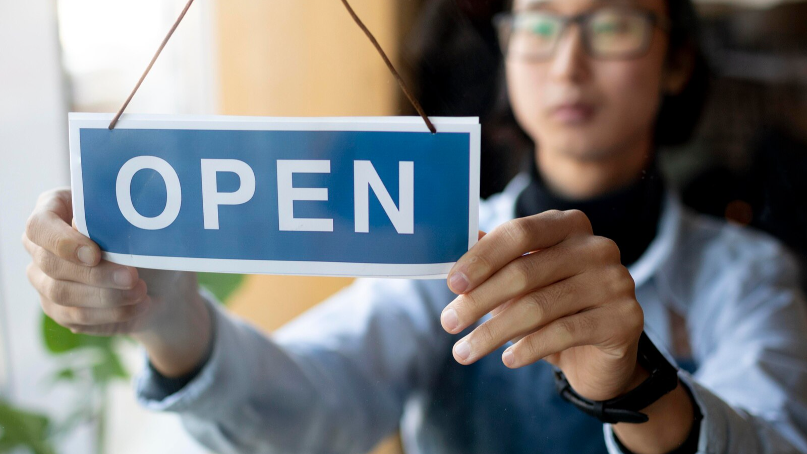 Person flips an OPEN sign on a storefront, showing how small business owners stay connected as they expand.