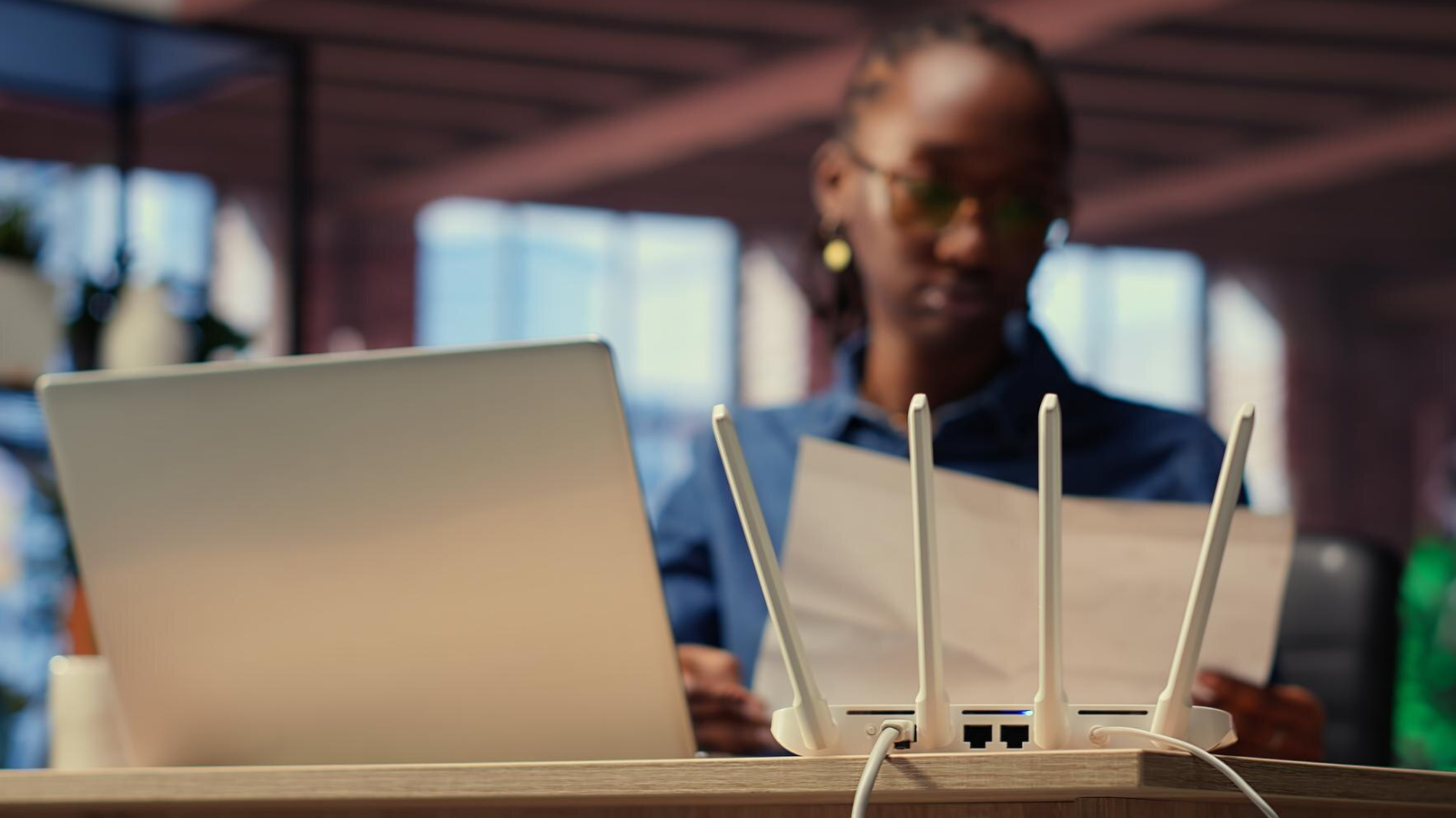 Wi-Fi router in focus with person working in background, representing dedicated Internet connection and professional installation for business needs.