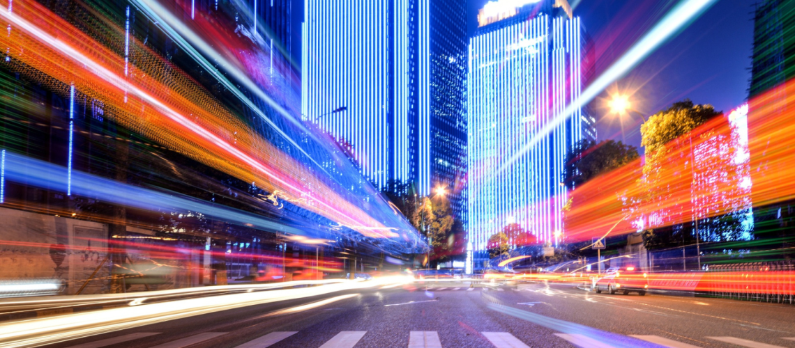 City street at night with vibrant light trails from moving vehicles and buildings illuminated in bright blue lights, symbolizing rapid digital data flow. This visual metaphor emphasizes the speed and efficiency of a fiber internet connection and high-speed fiber internet powered by an enterprise ISP.